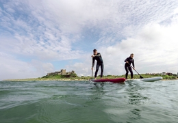 Two men on are paddleboarding in the sea with a heritage castle in the background.