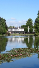 A large house overlooking a large garden complex and lake.