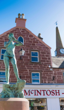 A metal statue of Peter Pan playing the flute in front of a shop