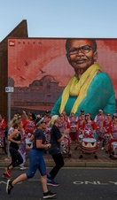 People running in front of a drumming band and colourful street art
