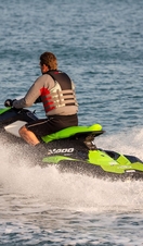 Middle aged man wearing a life vest rides a personal water craft Jet Ski along a calm sea.