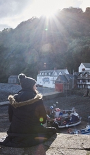 Woman sitting on harbour wall looking down on orw boats