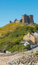 A castle on top of a hill beside a beach, surrounded by colourful buildings.