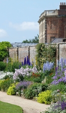 A walkway through a pretty walled garden blooming with flowers. 