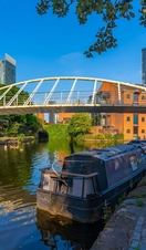 Bateau amarré sur un canal avec un pont piétonnier et des bâtiments urbains en arrière-plan