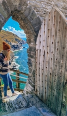 A woman stands at the top steps of a doorway at Tintagel with stunning coastline view beyond