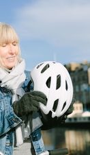 A woman putting on her bike helmet about to hop on a bike by the riverfront on a sunny day