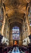 Inside Kings College Chapel, Cambridge, showing the fan vault ceiling and vast wooden panelling, with stain glass windows set above.