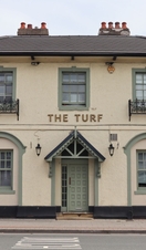 Entrance to a British pub with a sign that reads 'The Turf'. 