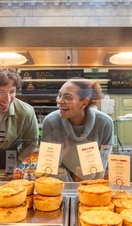 Friends admiring bakery pies through a glass divider.