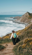 A woman walks along a coastal path with sea and headland in the distance