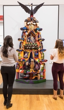 People admiring a sculpture of a totem pole in an art gallery. 