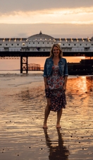 Woman standing on the beach near the pier at sunset