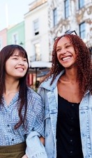 Two young women linking arms and walking in a street smiling