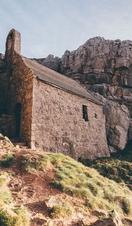 An old brick building on a hill, surrounded by cliffs. 