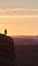 Silhouette of person hiking on large hill at sunset