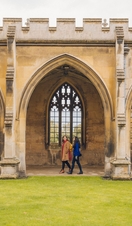 Two women walking under the arches of a college quad