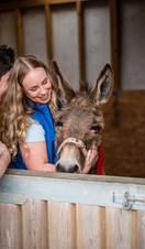 A man leans on a stable door while a woman smiles and strokes a donkey in a stable