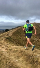 Trail runner running along a trail at the top of a steep hill