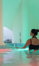 A woman in a black swimming costume in a relaxation pool with atmospheric lighting