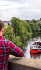 Two people stood on a bridge overlooking a tour boat sailing down a river in Durham