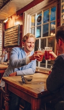 Two men toasting with pints in a bar in the evening