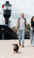 A man and a woman walk their dog in front of a large boat