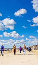 People walking along the coast next to colourful beach huts on a sunny day.