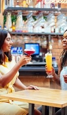 Two women sat at a table beside the bar, raising glasses