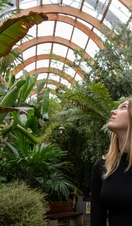 A woman walking past plants in a large temperate glasshouse