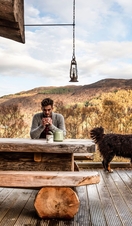 Man sitting on the terrace of a wooden lodge with large St Bernard dog, Scottish Highlands 