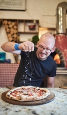 Man sitting at table, sprinkling cheese on pizza