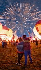 Lit up hot air balloons and fireworks in the night sky