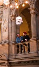 Two men looking at installation of suspended head sculptures