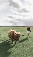 Girl, in a white skirt, walking beside a Highland cow