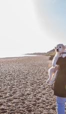 A woman carrying a dog along a beach in Dunwich