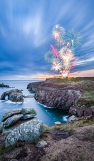 Firework display seen from across a rocky headland at twilight