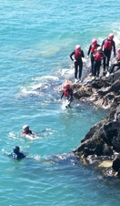 A group of people diving into the ocean off a rock coast in Cardiff, Wales