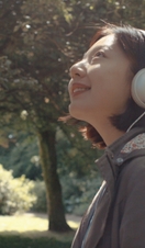 A woman in headphones looking out in a garden at St Fagans National Museum of History, Cardiff