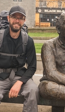 A man with walking sticks posing next to a statue on a bench in Glasgow