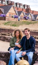 Two people sitting and listening to a tour guide on a Roman themed tour of Chester