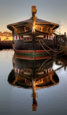 Heritage boat docked in a city harbour at dusk.