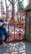 Two women pose in front of the red gates at the Strawberry Field garden.
