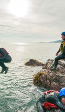 People coasteering off rocks into the ocean.