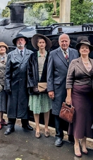 Actors in costume in front of a steam train as part of a murder mystery performance