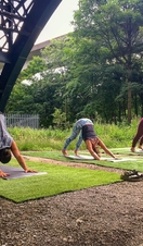 People practising yoga outside, beneath a bridge