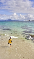 A high angle view of an independent young woman walking on the white sand with the crystal clear blue waters of Iona, Scotland