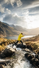 A man jumping across a stream whilst hiking