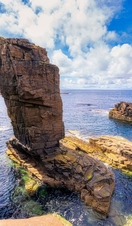 Man straddling two sea stacks overlooking a rocky outcrop and the ocean