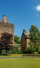 Exterior of a small castle with a flagpole and a few trees on a sunny day.